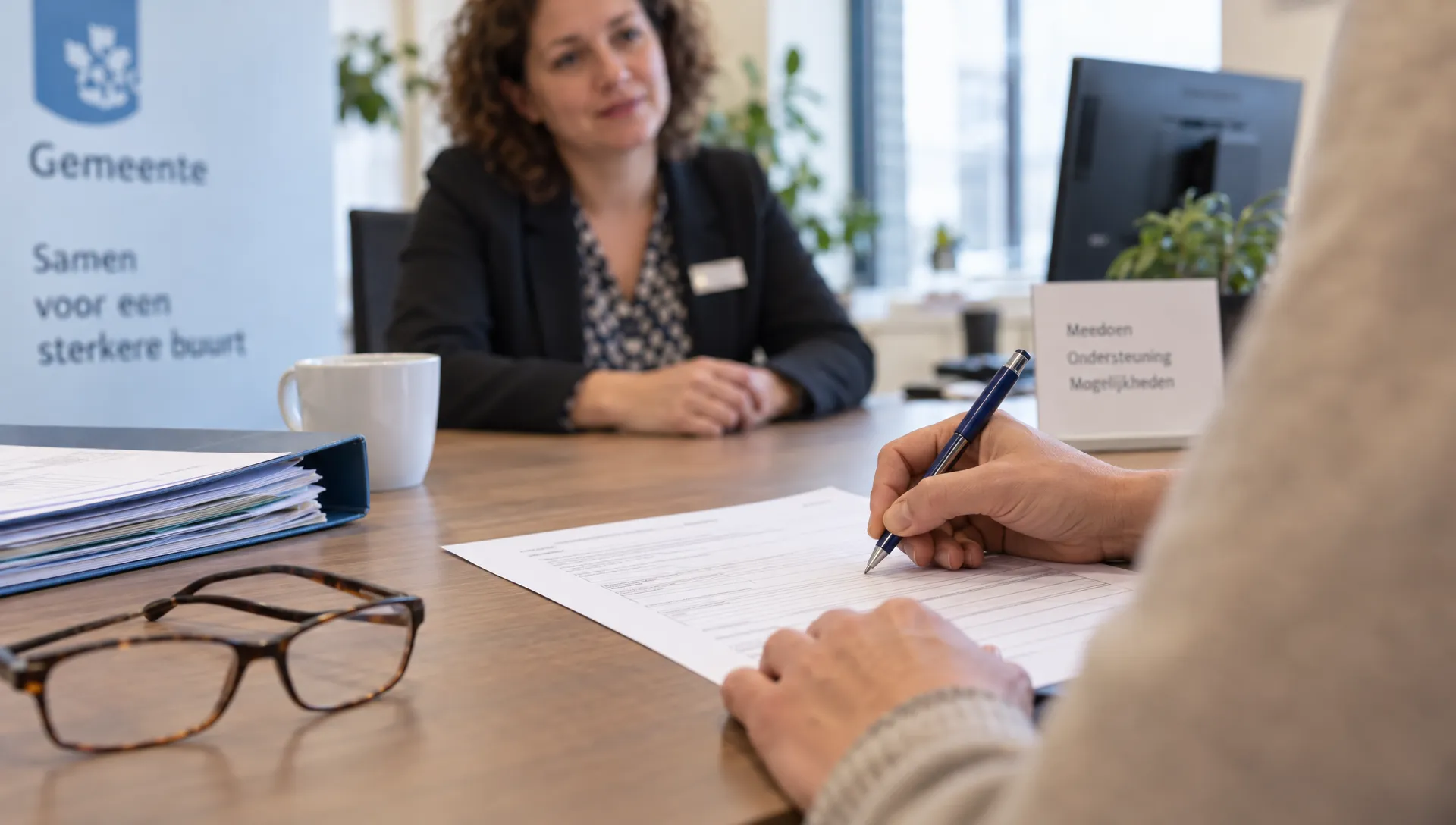 Een hand vult tijdens een gesprek in een gemeentelijke spreekkamer een formulier in over de benodigde begeleiding voor dagbesteding.